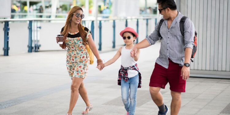 Happy stylish parents holding hands with daughter walking on street in the city