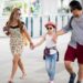 Happy stylish parents holding hands with daughter walking on street in the city