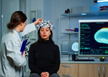 Neurological doctor cheking eeg headset explaining to patient diagnosis of disease and treatment for nervous system. Scientist researcher analysing brain scan and tomography on monitor in lab