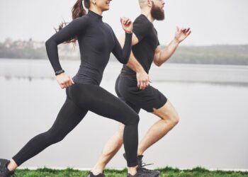 Couple jogging and running outdoors in park near the water. Young bearded man and woman exercising together in morning.