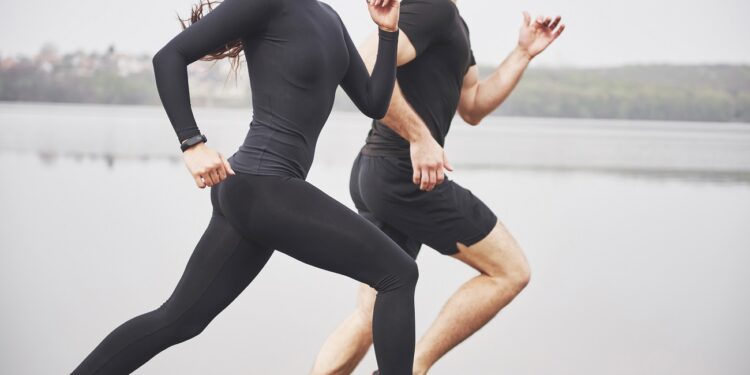Couple jogging and running outdoors in park near the water. Young bearded man and woman exercising together in morning.