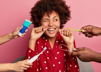 oral hygiene and teeth care concept. curly haired woman cleans teeth with floss, cleans tongue with cleaner, uses toothbrush and toothpaste, poses at home, wears nightwear, has perfect healthy tooth