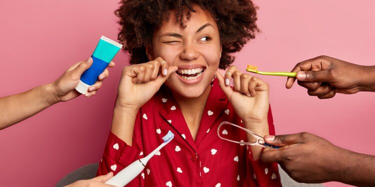 oral hygiene and teeth care concept. curly haired woman cleans teeth with floss, cleans tongue with cleaner, uses toothbrush and toothpaste, poses at home, wears nightwear, has perfect healthy tooth