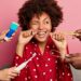 oral hygiene and teeth care concept. curly haired woman cleans teeth with floss, cleans tongue with cleaner, uses toothbrush and toothpaste, poses at home, wears nightwear, has perfect healthy tooth
