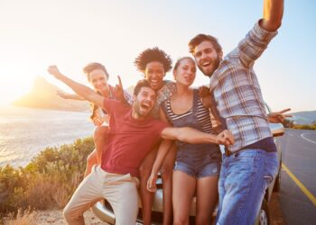 group,of,friends,standing,by,car,on,coastal,road,at