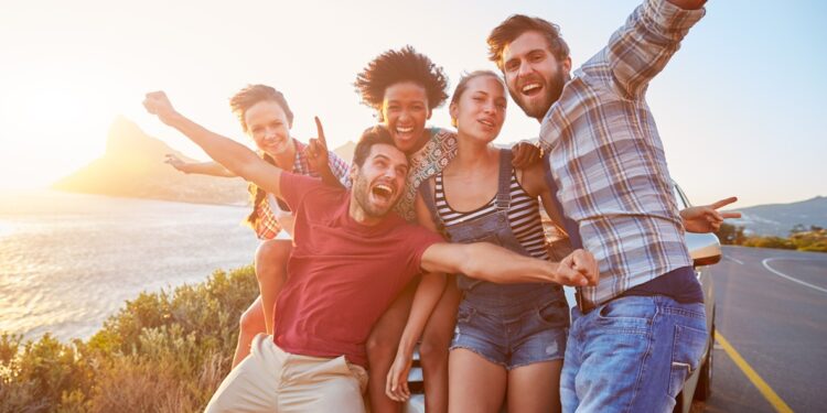 group,of,friends,standing,by,car,on,coastal,road,at