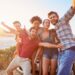 group,of,friends,standing,by,car,on,coastal,road,at