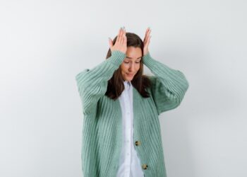 young lady keeping hands on head in blouse, cardigan and looking wistful , back view.