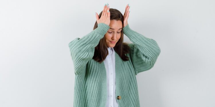 young lady keeping hands on head in blouse, cardigan and looking wistful , back view.