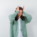 young lady keeping hands on head in blouse, cardigan and looking wistful , back view.