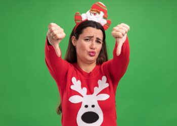 unpleased young beautiful girl wearing christmas sweater with christmas hair hoop showing thumbs down isolated on green background