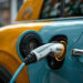 an orange and blue electric car charging on a street, themes of green and eco friendly energy alternatives for vehicles and co2 emission reduction.
