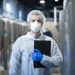 technologist with protective mask and hairnet standing at factory production line.
