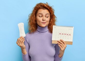 photo of young woman looks at period calendar, checks menstruation days, holds soft sanitary pad, puzzled with delay of periods, has premesntrual syndrom as intense mood swings, prepares for pms