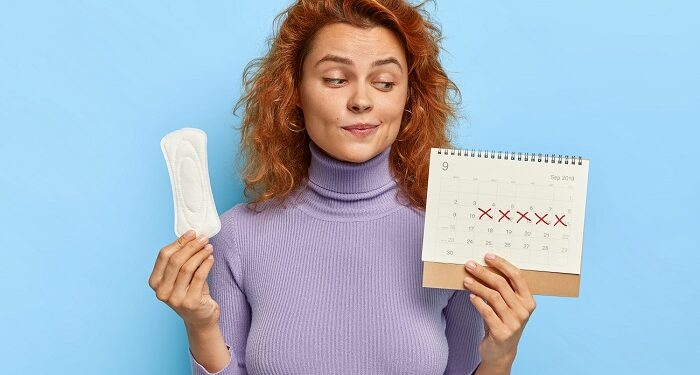 photo of young woman looks at period calendar, checks menstruation days, holds soft sanitary pad, puzzled with delay of periods, has premesntrual syndrom as intense mood swings, prepares for pms
