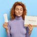 photo of young woman looks at period calendar, checks menstruation days, holds soft sanitary pad, puzzled with delay of periods, has premesntrual syndrom as intense mood swings, prepares for pms
