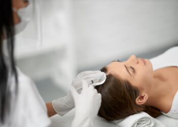 beautician in protective mask doing procedure for hair.