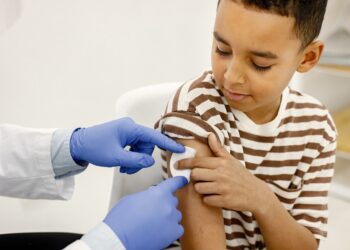 male doctor holding a cotton on a boy's shoulders after a vaccin