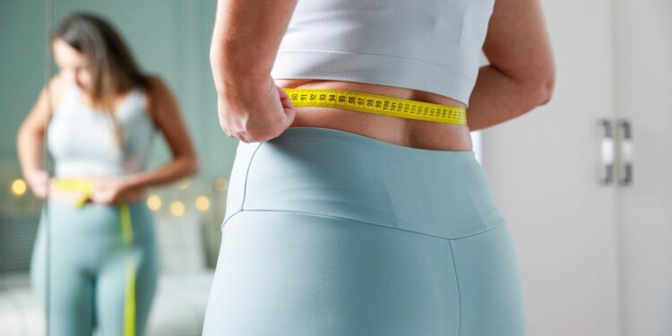 young woman taking measurements of her body in front of the mirr
