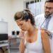 young female patient in the clinic suffered from pneumonia, she is coughing the doctor listens to the wheezing in the lungs with a stethoscope.
