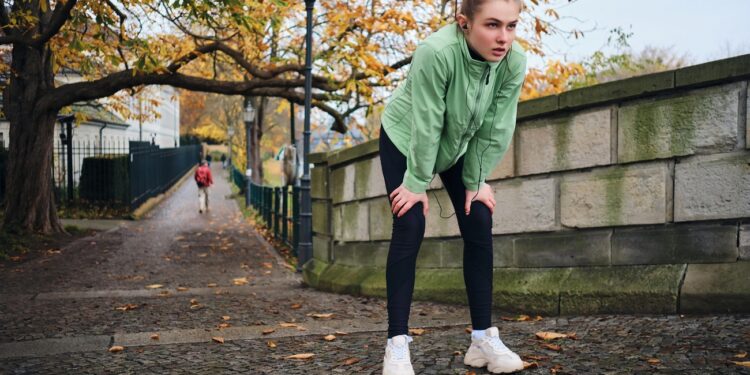 tired sporty girl resting after run in beautiful autumn city park