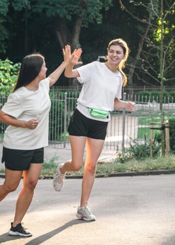 two young adult woman running in a park.