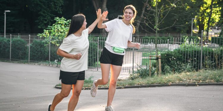 two young adult woman running in a park.
