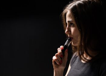 attractive young woman vaping and blowing smoke isolated on black background