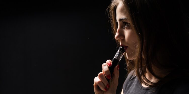 attractive young woman vaping and blowing smoke isolated on black background