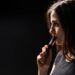 attractive young woman vaping and blowing smoke isolated on black background