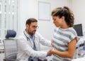 patient telling physician about her pain and health problems during visit to hospital. young woman complaining about back or kidney ache while sitting on examination bed at the doctor's office