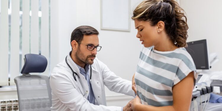 patient telling physician about her pain and health problems during visit to hospital. young woman complaining about back or kidney ache while sitting on examination bed at the doctor's office