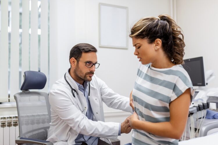 patient telling physician about her pain and health problems during visit to hospital. young woman complaining about back or kidney ache while sitting on examination bed at the doctor's office
